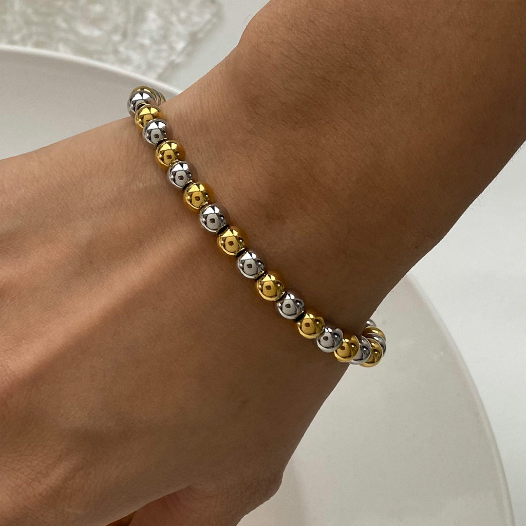 Bracelet with gold and silver beads on a wrist against a neutral background