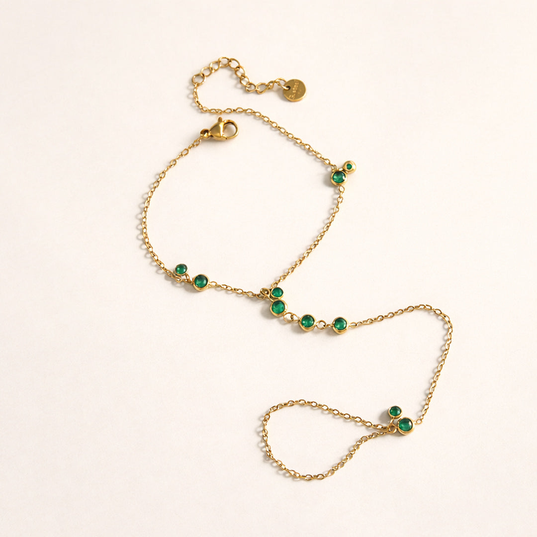 Gold-plated emerald station hand chain on a model hand, ring-to-wrist chain bracelet with green stones.