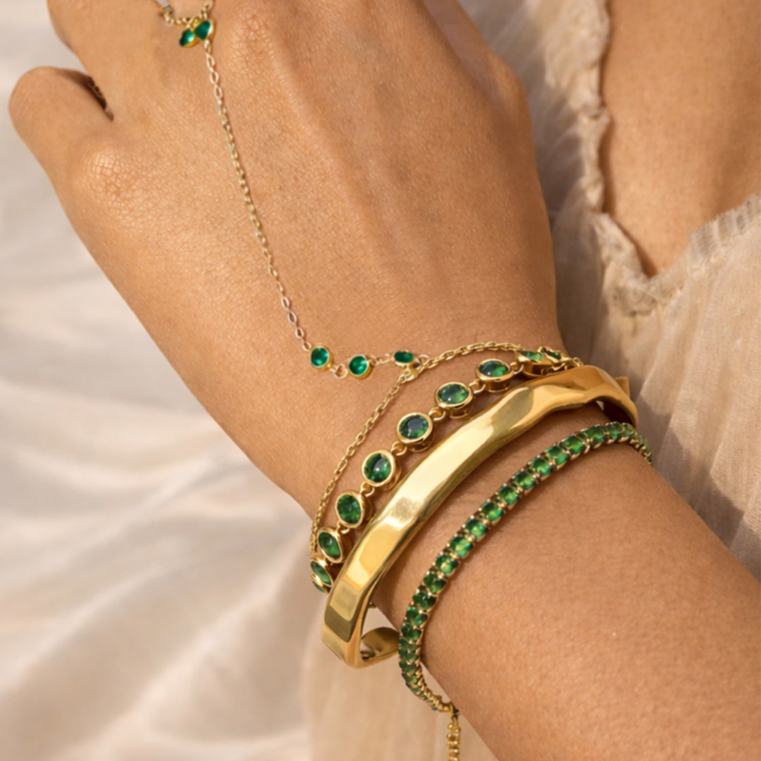 Gold bracelets with green gemstones on a hand against a neutral background