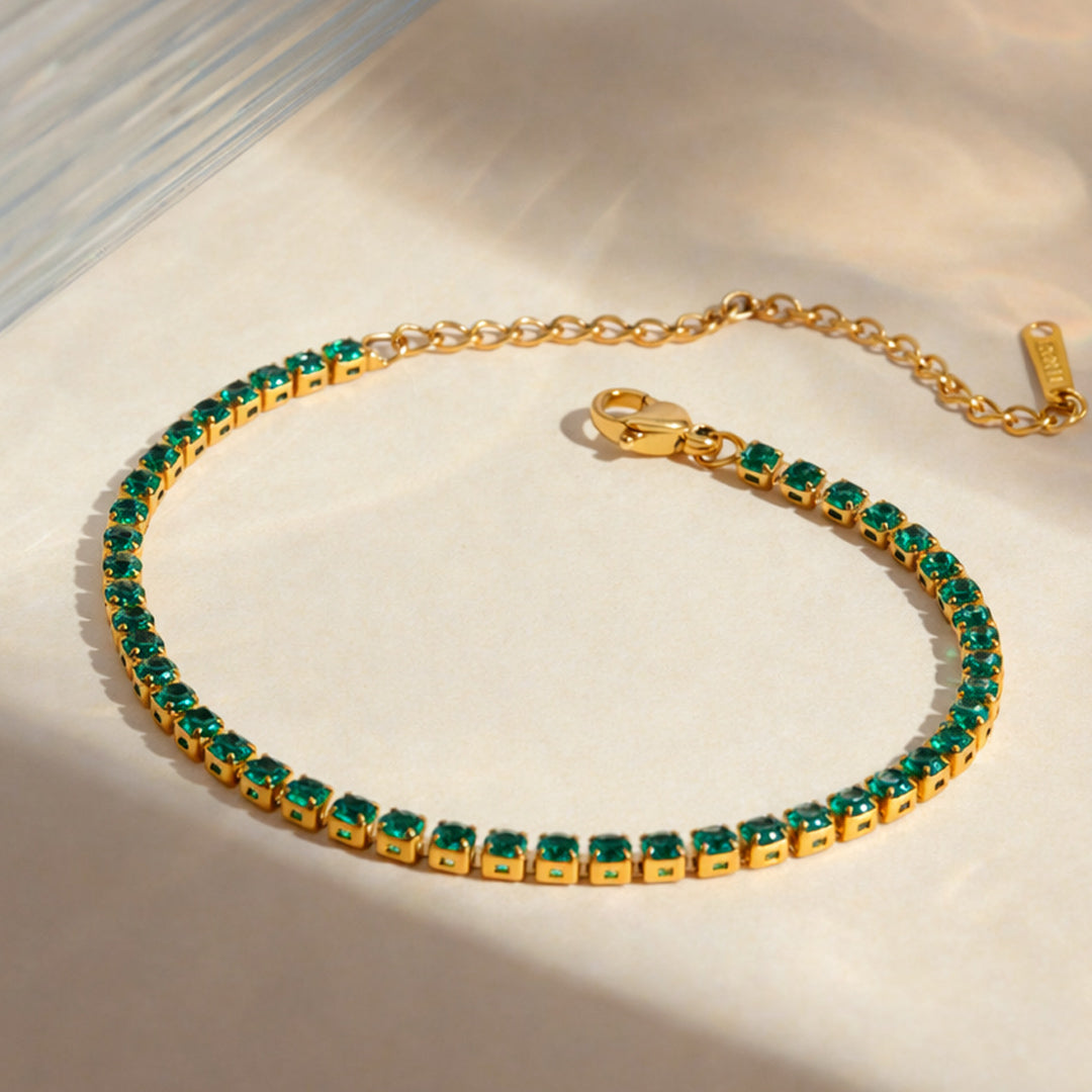 Gold tennis bracelet with emerald green stones from OROR Parure displayed on ivory background.