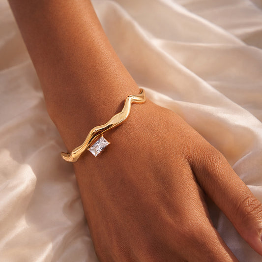 Woman wearing a gold wave bangle with baguette-cut clear zircon accent