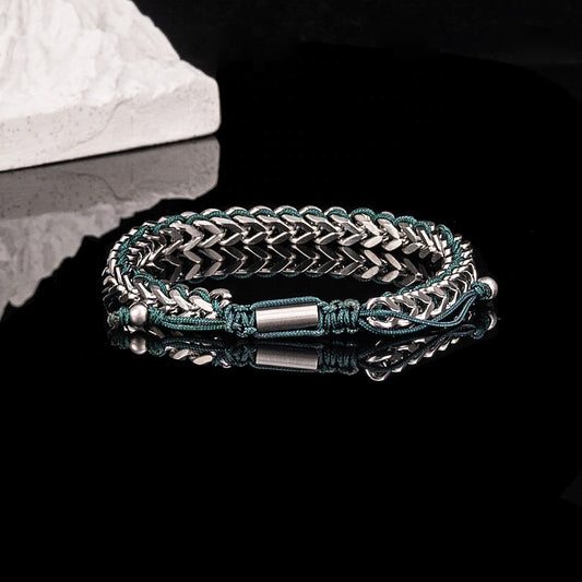 Stainless steel chain bracelet with green cord detail, product view on dark background