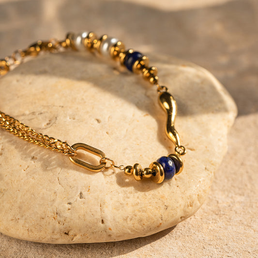 Gold bracelet with lapis blue accents, product view on stone surface