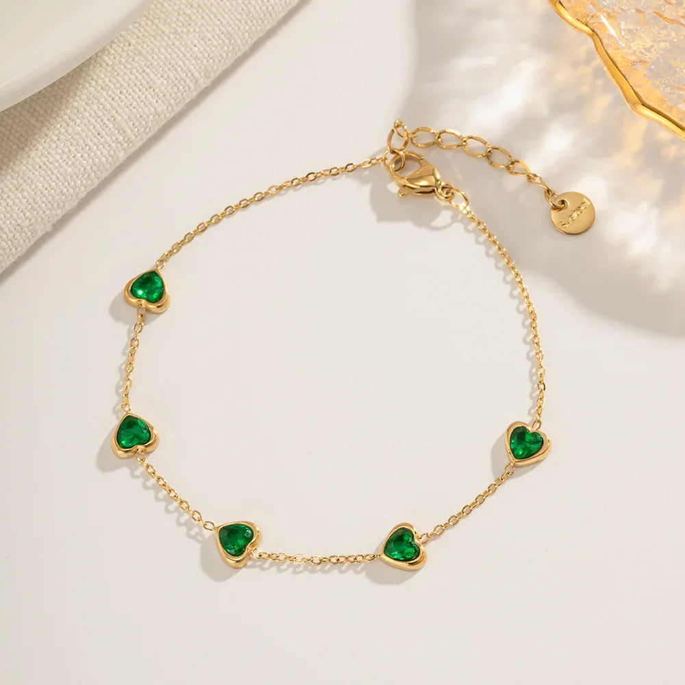 Emerald heart contour bracelet flat lay, green heart stones in polished gold frame with adjustable chain