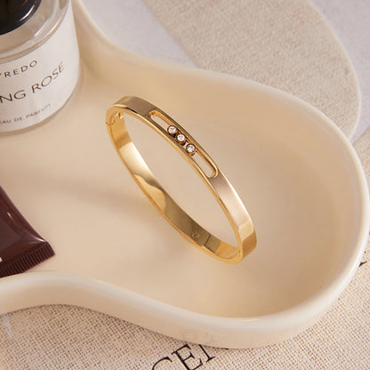 Gold bracelet with small diamonds on a white dish with a perfume bottle in the background
