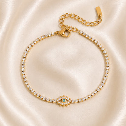 Gold tennis bracelet with a turquoise eye centerpiece and zircon accents displayed on ivory satin in OROR luxury styling.