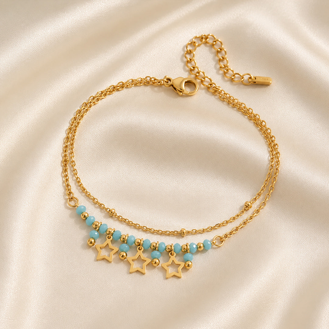 Gold bracelet featuring turquoise beads and three open star charms displayed on an ivory satin background.