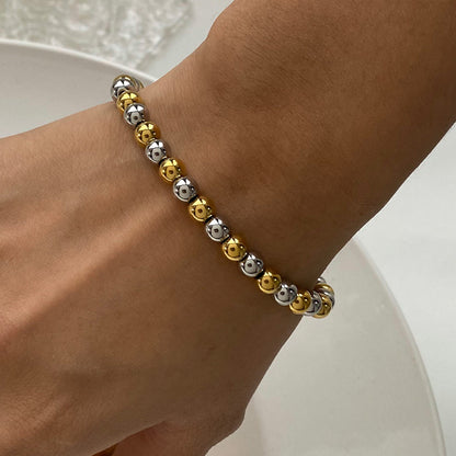 Bracelet with gold and silver beads on a wrist against a neutral background