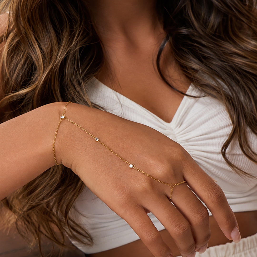 Woman wearing the Étoile gold handchain with sparkling zircon accents, styled with a white crop top and flowing hair in OROR luxury photography.