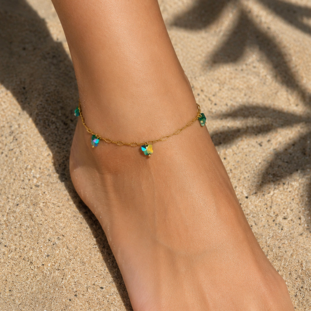 Gold anklet with green beads on a foot against a sandy background