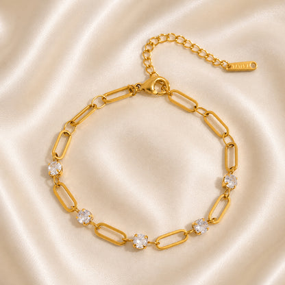 Gold bracelet with zircon accents and elongated links displayed on ivory satin in OROR luxury styling.