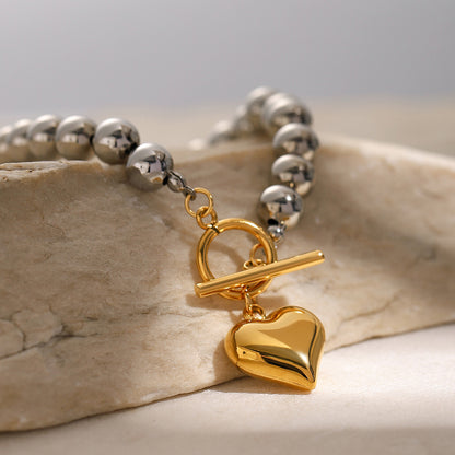 Silver beaded bracelet with a gold heart charm on a stone surface