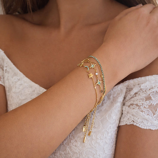 Gold-plated layered chain bracelet stack on wrist, turquoise zircon details