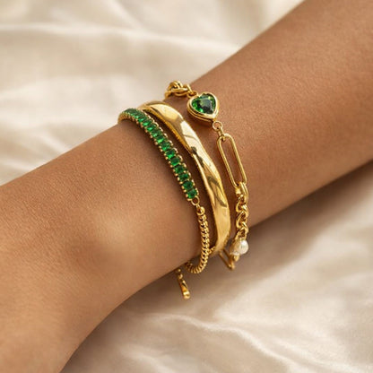Three-piece emerald and gold bracelet set featuring a sculpted gold cuff, emerald stone bracelet, and chain-link bracelet worn on wrist.