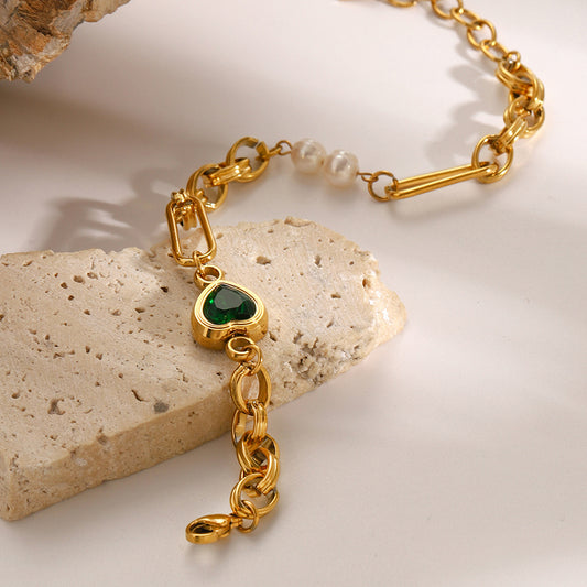 Gold bracelet with a heart-shaped green gemstone on a stone surface