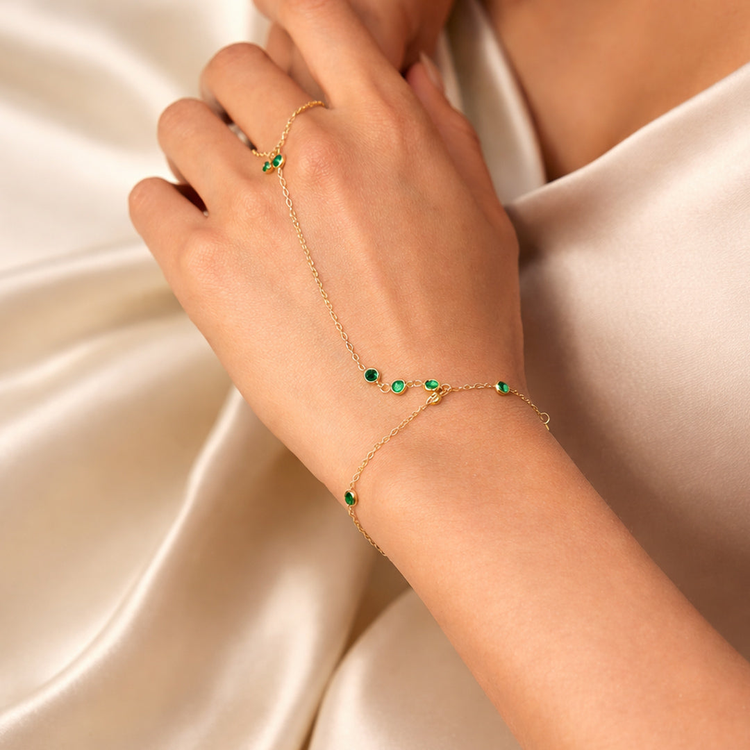 Gold-plated emerald station hand chain on a model hand, ring-to-wrist chain bracelet with green stones.