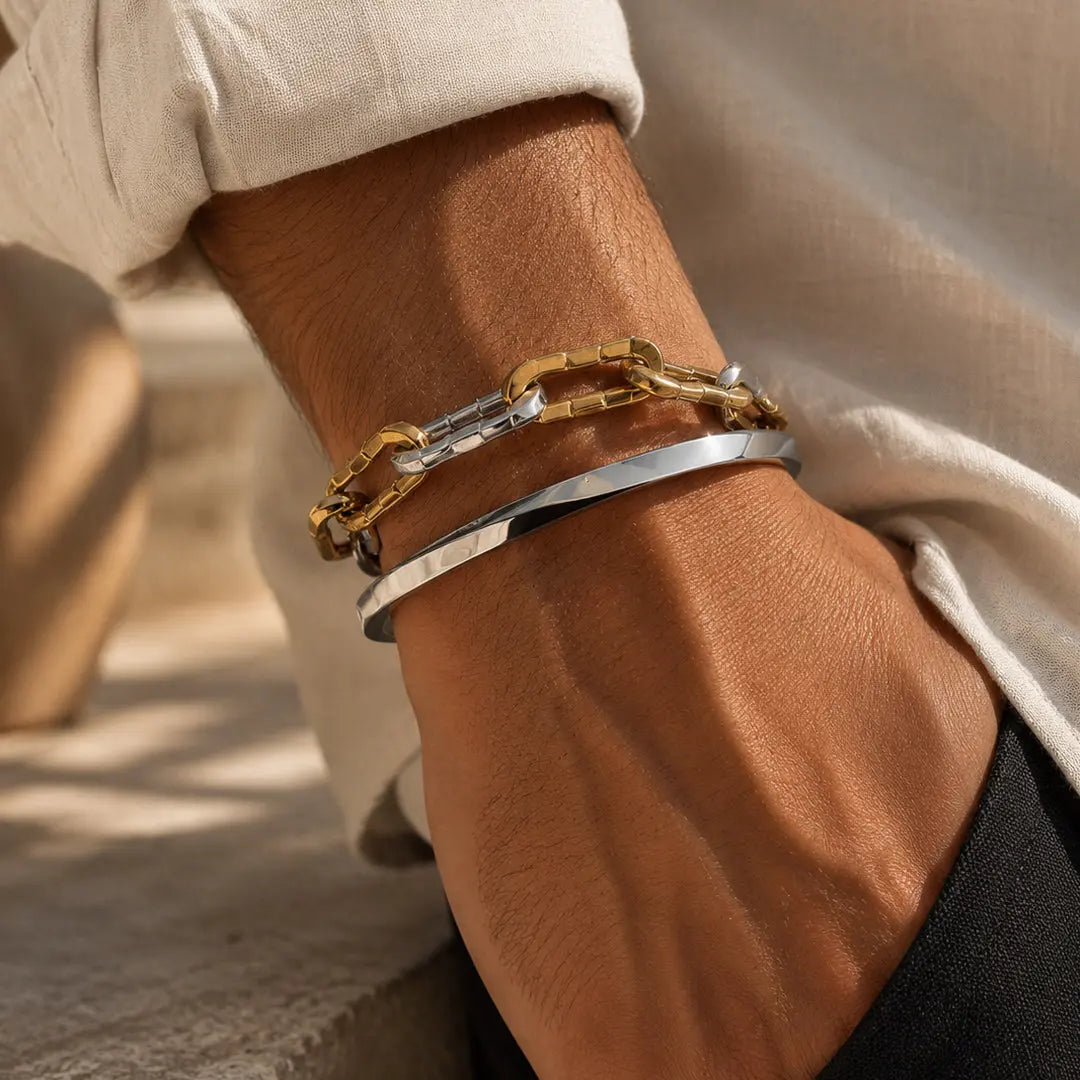 Close-up of a wrist wearing two gold and silver chain bracelets on a neutral background.
