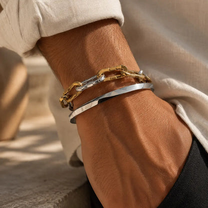 Close-up of a wrist wearing two gold and silver chain bracelets on a neutral background.