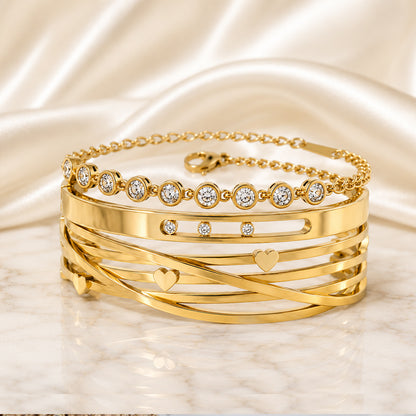 Amour Signature Stack featuring a gold heart cuff with bezel-set crystals paired with a delicate crystal tennis bracelet on an ivory satin and marble background.