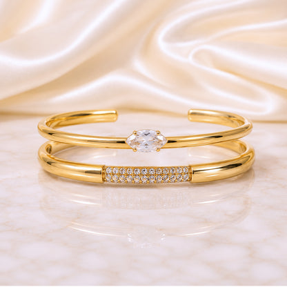 Two-piece gold cuff stack featuring a marquise zircon cuff and pavé crystal cuff displayed on an ivory satin background.