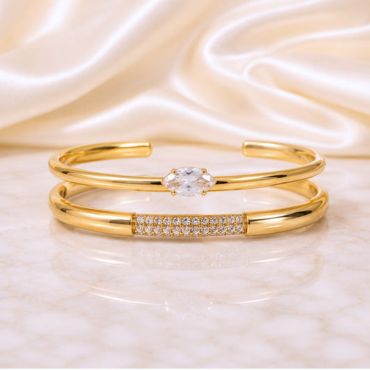 Two-piece gold cuff stack featuring a marquise zircon cuff and pavé crystal cuff displayed on an ivory satin background.