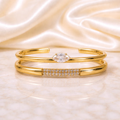 Two-piece gold cuff stack featuring a marquise zircon cuff and pavé crystal cuff displayed on an ivory satin background.