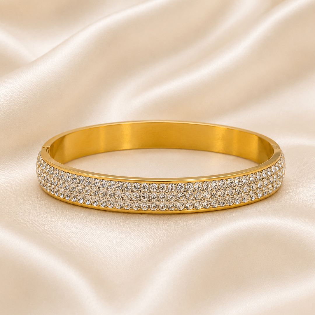 18K gold PVD bangle with five rows of pavé-set cubic zirconia displayed on an ivory satin background.