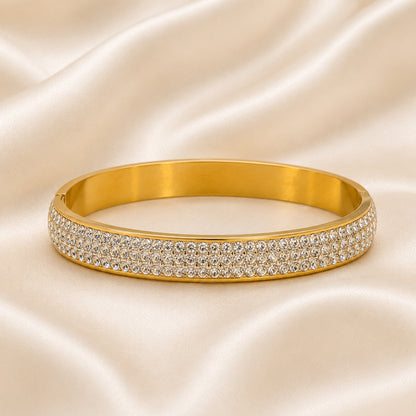 18K gold PVD bangle with five rows of pavé-set cubic zirconia displayed on an ivory satin background.