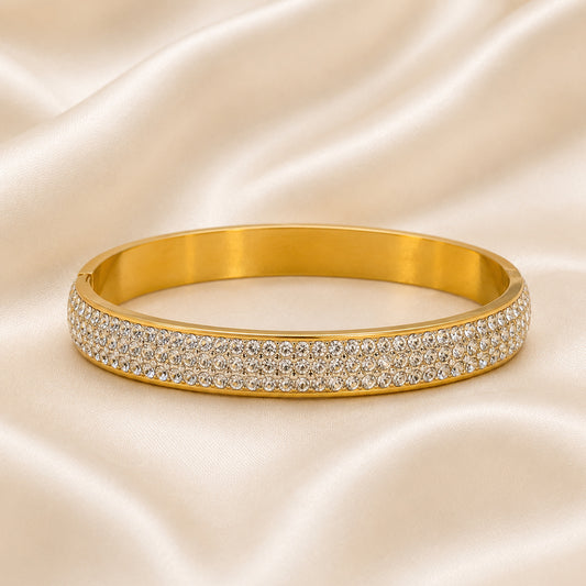 18K gold PVD bangle with five rows of pavé-set cubic zirconia displayed on an ivory satin background.