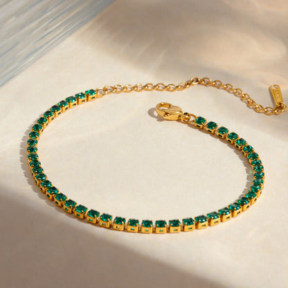 Gold tennis bracelet with emerald green stones from OROR Parure displayed on ivory background.