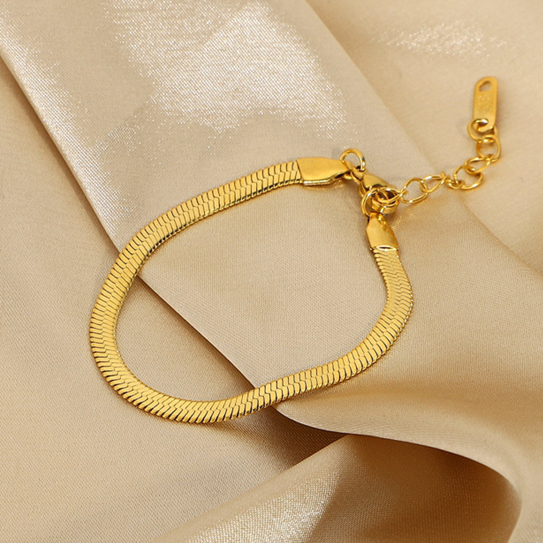Gold herringbone bracelet from OROR Parure displayed on ivory satin background.