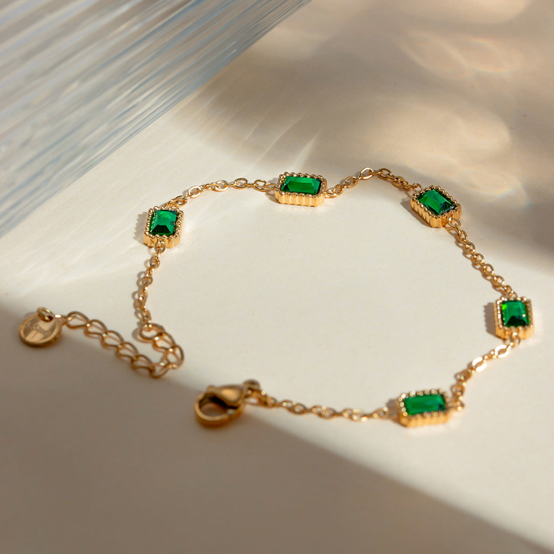 Gold station bracelet with spaced emerald-cut green stones on neutral ivory background from OROR Parure.