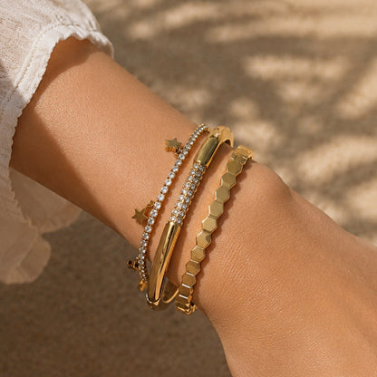 Three-piece gold bracelet stack featuring a geometric faceted bangle, pavé zircon cuff, and star charm tennis bracelet.