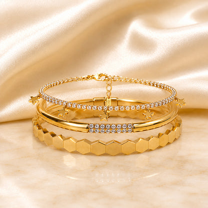 Three-piece gold bracelet stack featuring a geometric faceted bangle, pavé zircon cuff, and star charm tennis bracelet on an ivory satin background.