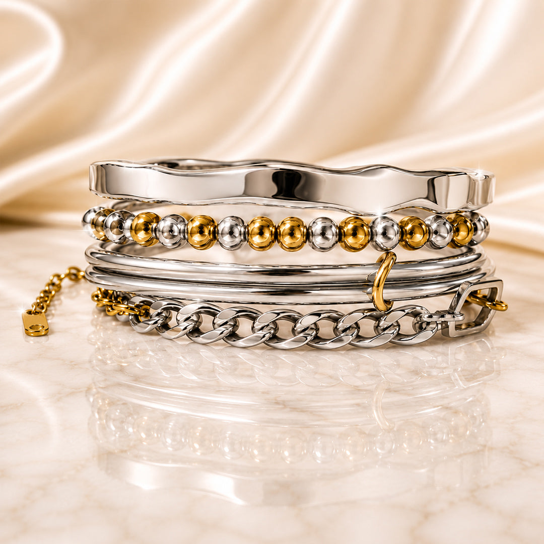 Four-piece mixed-metal bracelet stack featuring a sculptural silver cuff, beaded bracelet, layered wire bracelet, and curb chain displayed on ivory satin and marble.
