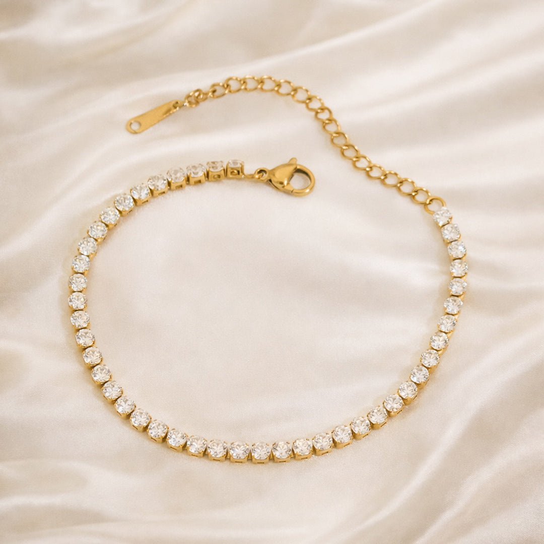Gold tennis bracelet with clear zircon stones on an ivory satin background