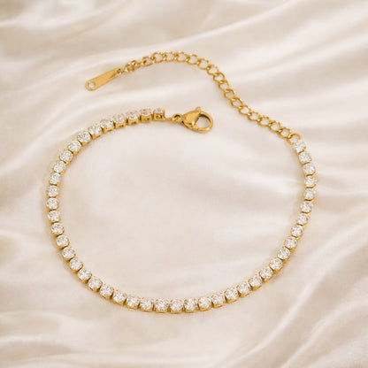 Gold tennis bracelet with clear zircon stones on an ivory satin background