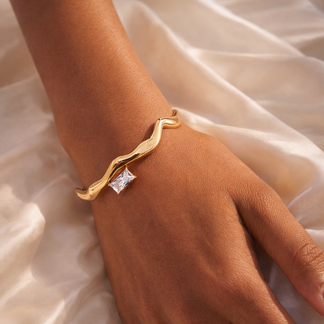 Woman wearing a gold wave bangle with baguette-cut clear zircon accent