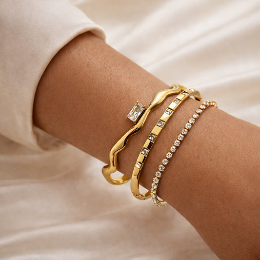 Woman wearing a three-piece gold-plated zircon bracelet set: sculptural cuff, bezel bangle, and slim tennis bracelet.