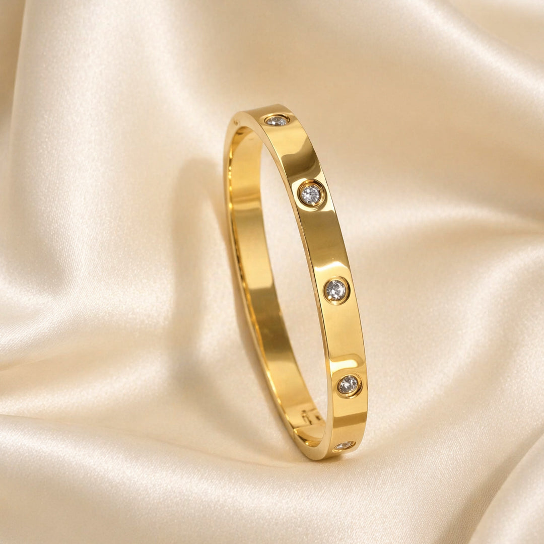 Gold bangle with bezel-set clear zircon stones on ivory satin background