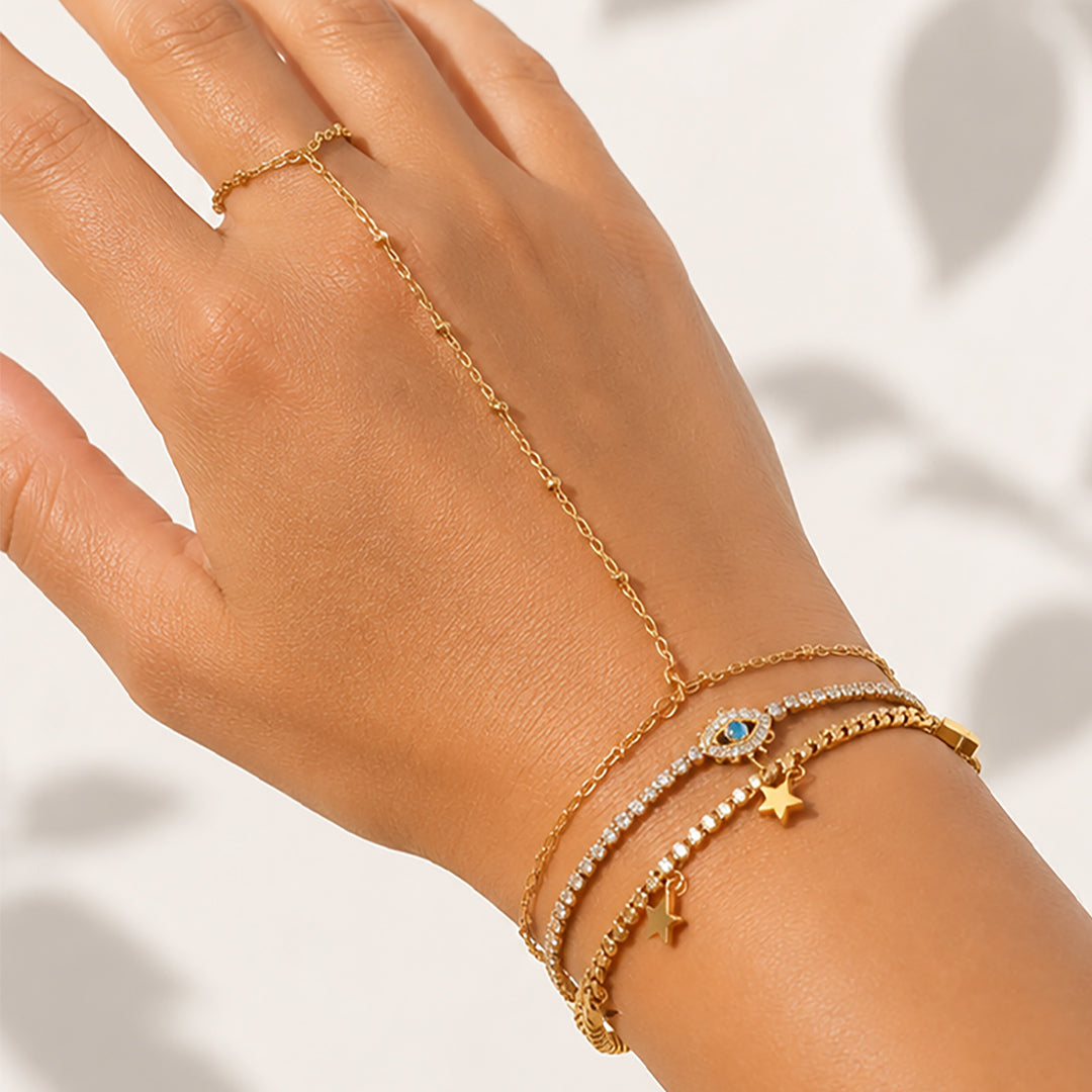 Gold handchain stack with pavé bracelet, star charms, and evil-eye detail worn elegantly on a woman's hand.