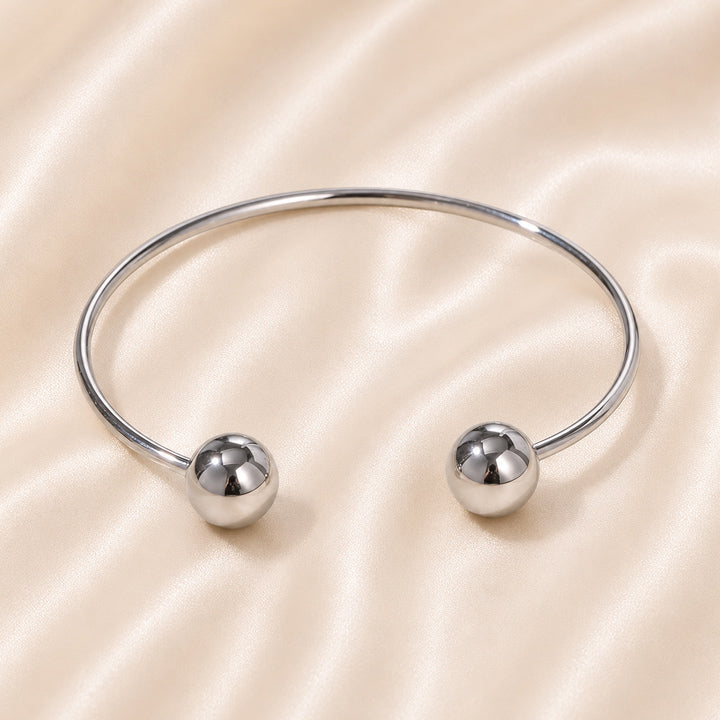 Silver bangle with spherical ends on a beige satin background