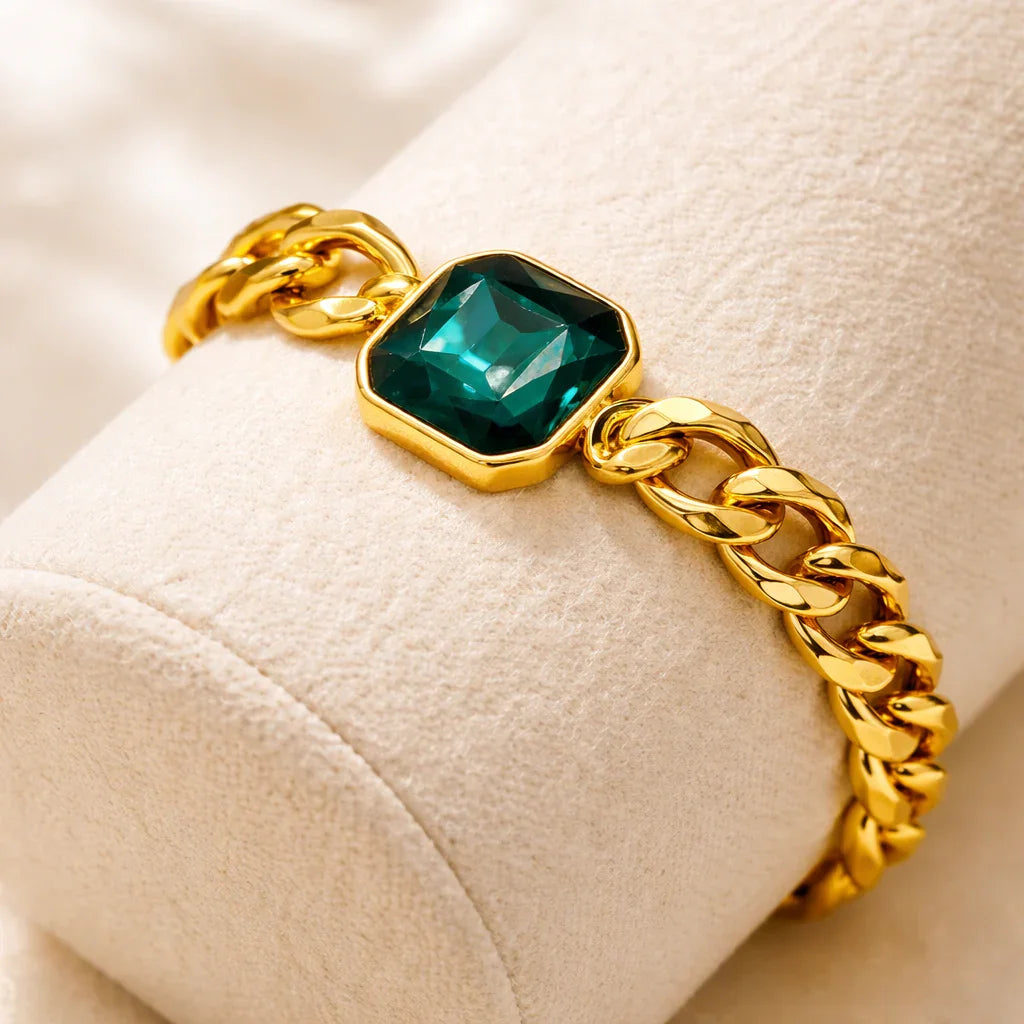 Close-up of emerald faceted stone in polished bezel on gold chain bracelet, product detail view