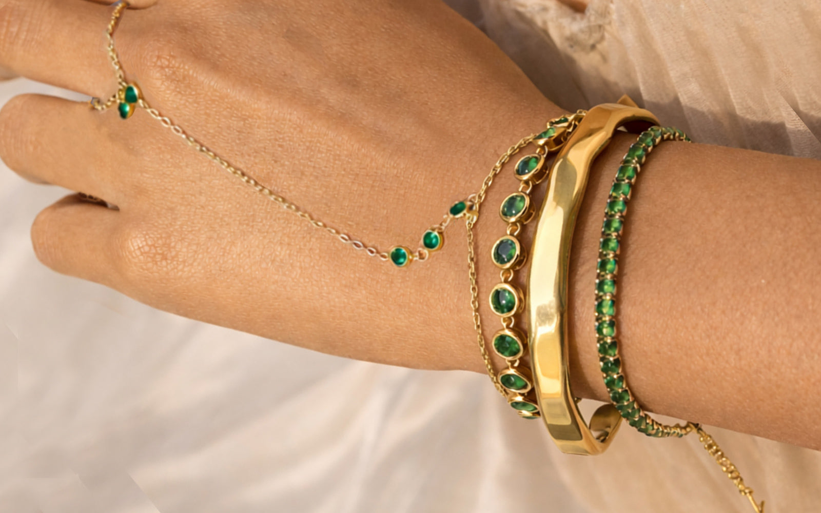 Gold and green gemstone bracelets on a wrist against a neutral background