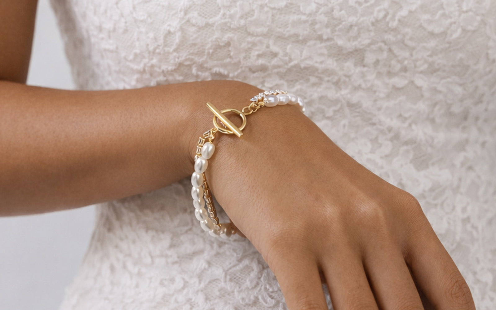 Hand wearing a pearl bracelet with a gold clasp on a neutral background
