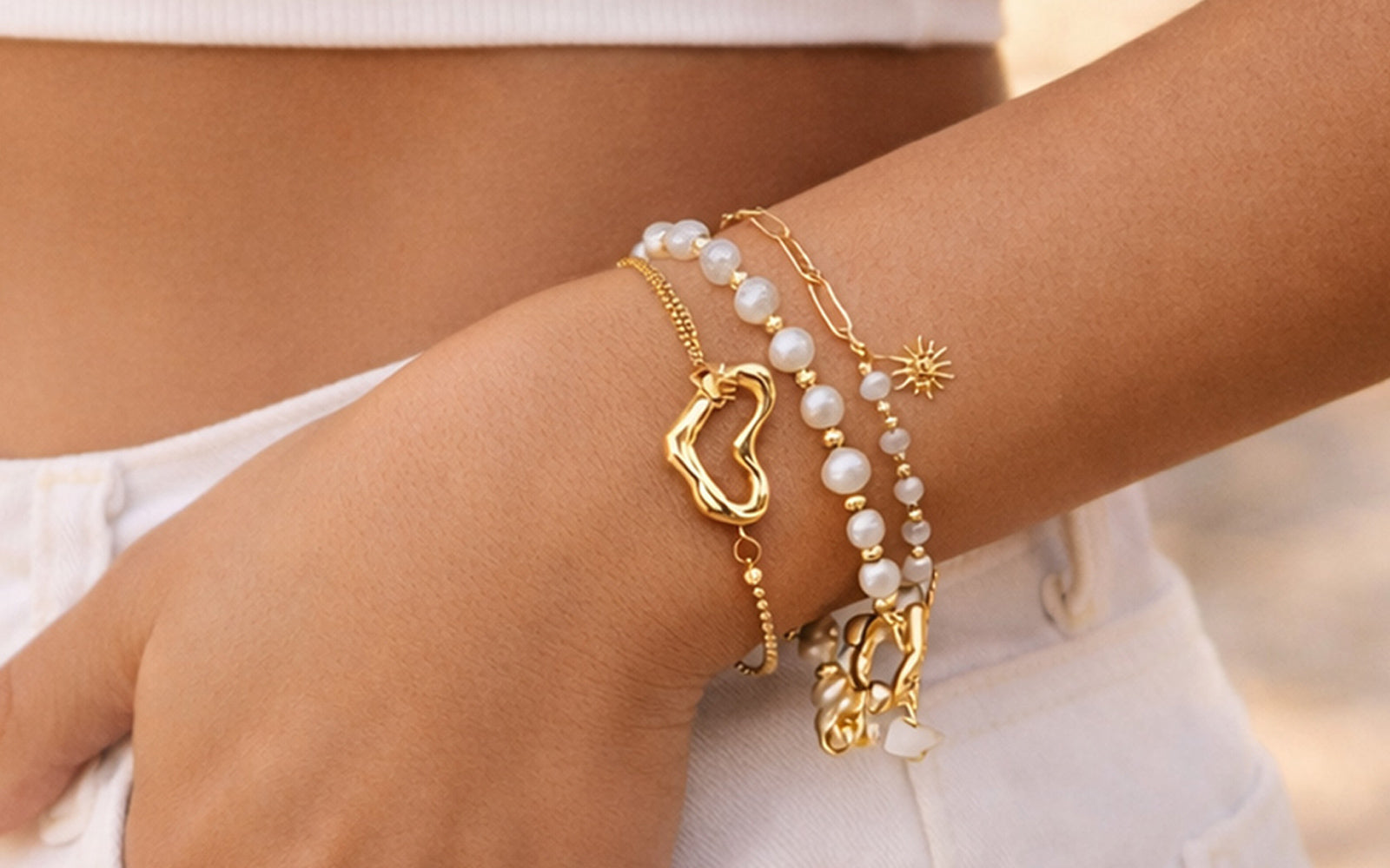 Close-up of a wrist wearing multiple gold and pearl bracelets against a neutral background.