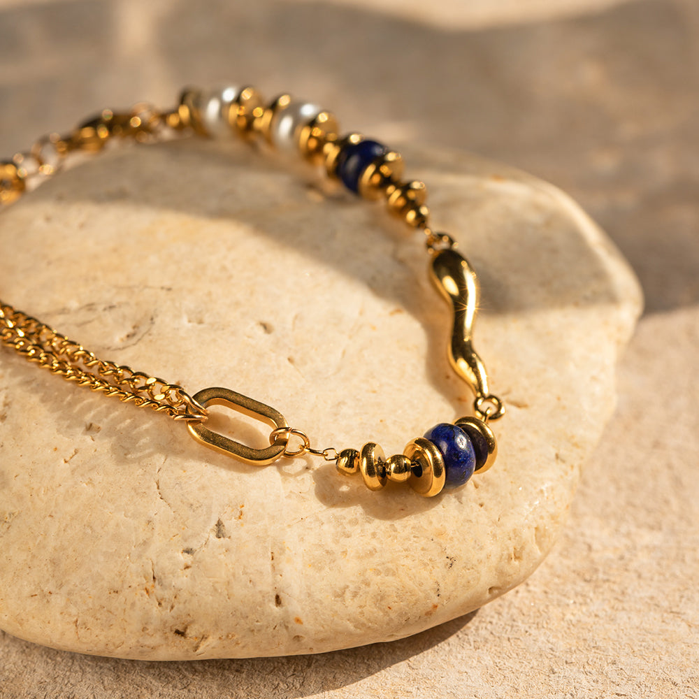 Gold bracelet with lapis blue accents, product view on stone surface