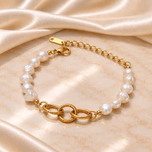 A gold chain bracelet with irregular white freshwater pearls and a central twisted rope link motif, displayed on a draped champagne satin fabric.