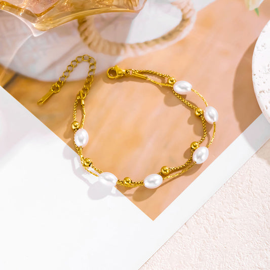 A gold chain bracelet with irregular white freshwater pearls and small gold beads, styled on a beige and white paper background.