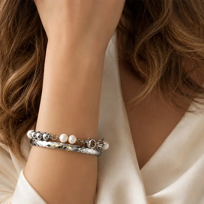 Close-up of a wrist wearing a silver bracelet with pearls, against a neutral background.